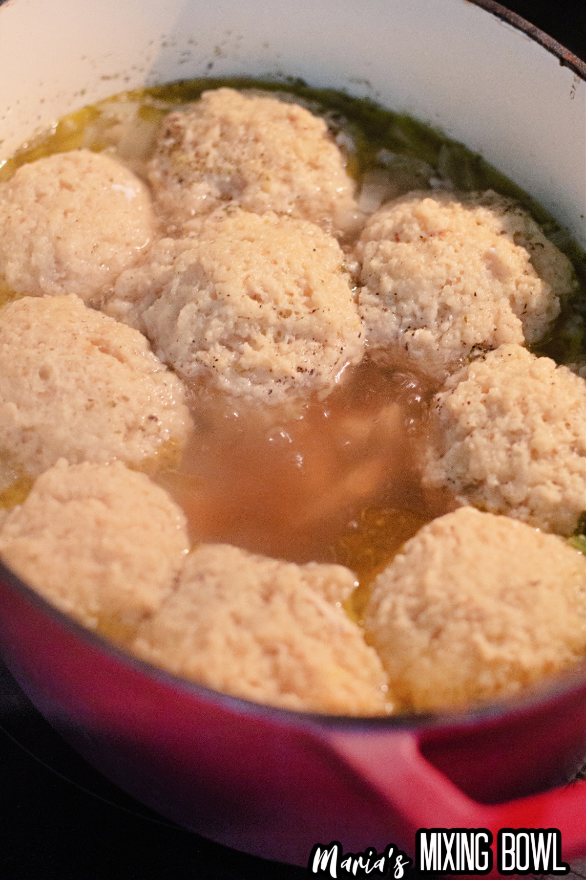 matzo balls being added to the soup in a dutch oven.