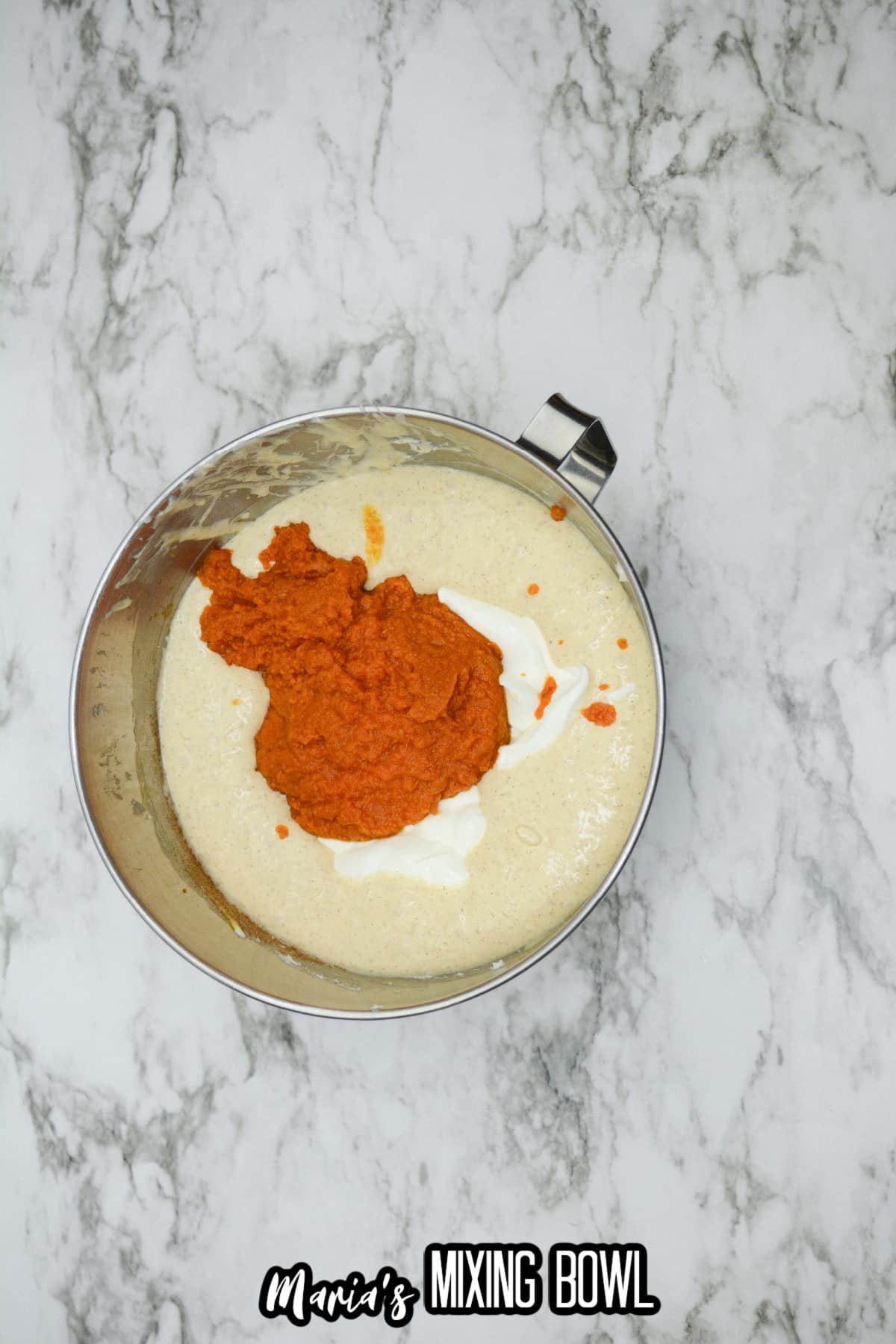canned pumpkin being added to a cream cheese mixture in a stainless steel mixing bowl.