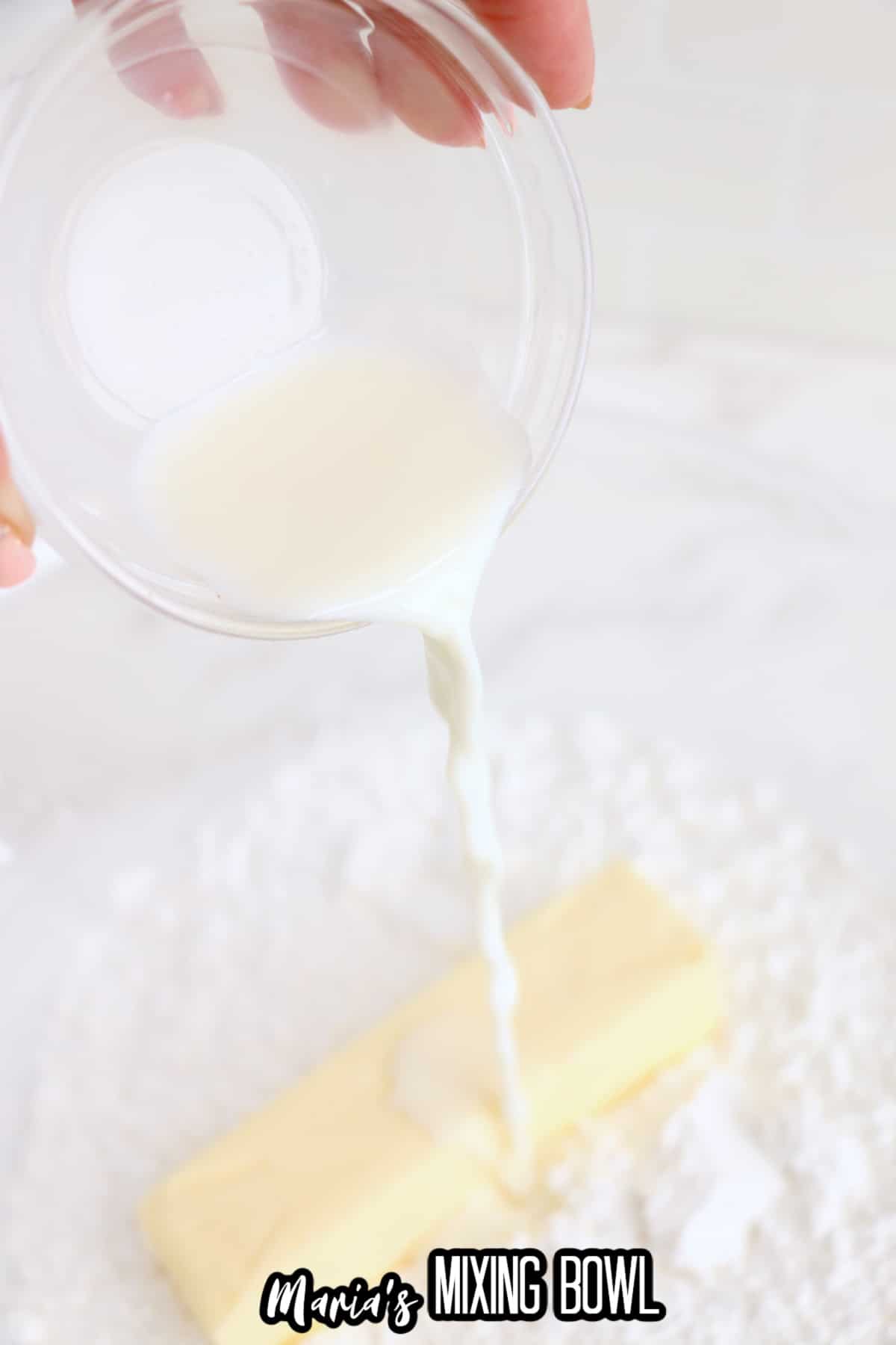 heavy cream, butter, and powdered sugar being mixed in a glass mixing bowl.