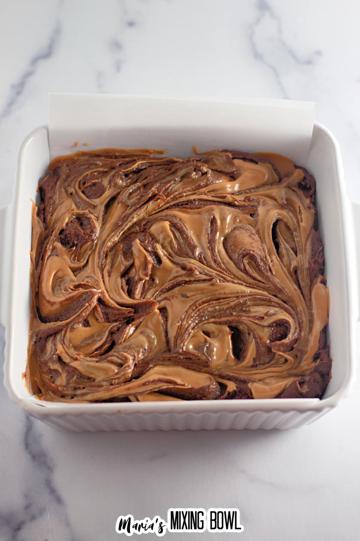 peanut butter being swirled into the brownie batter in a square baking dish.
