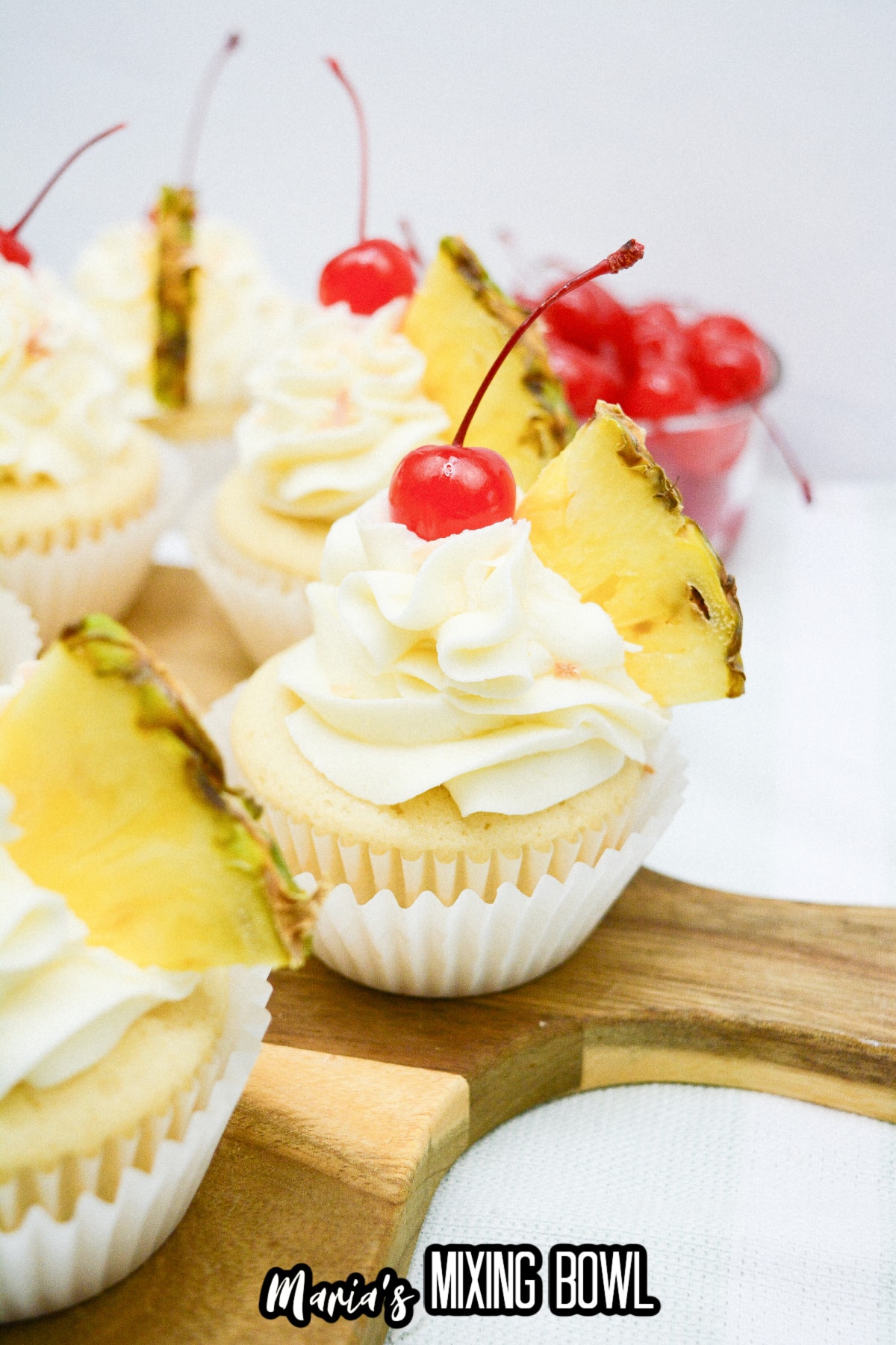 pina colada cupcakes on a wooden cutting board.