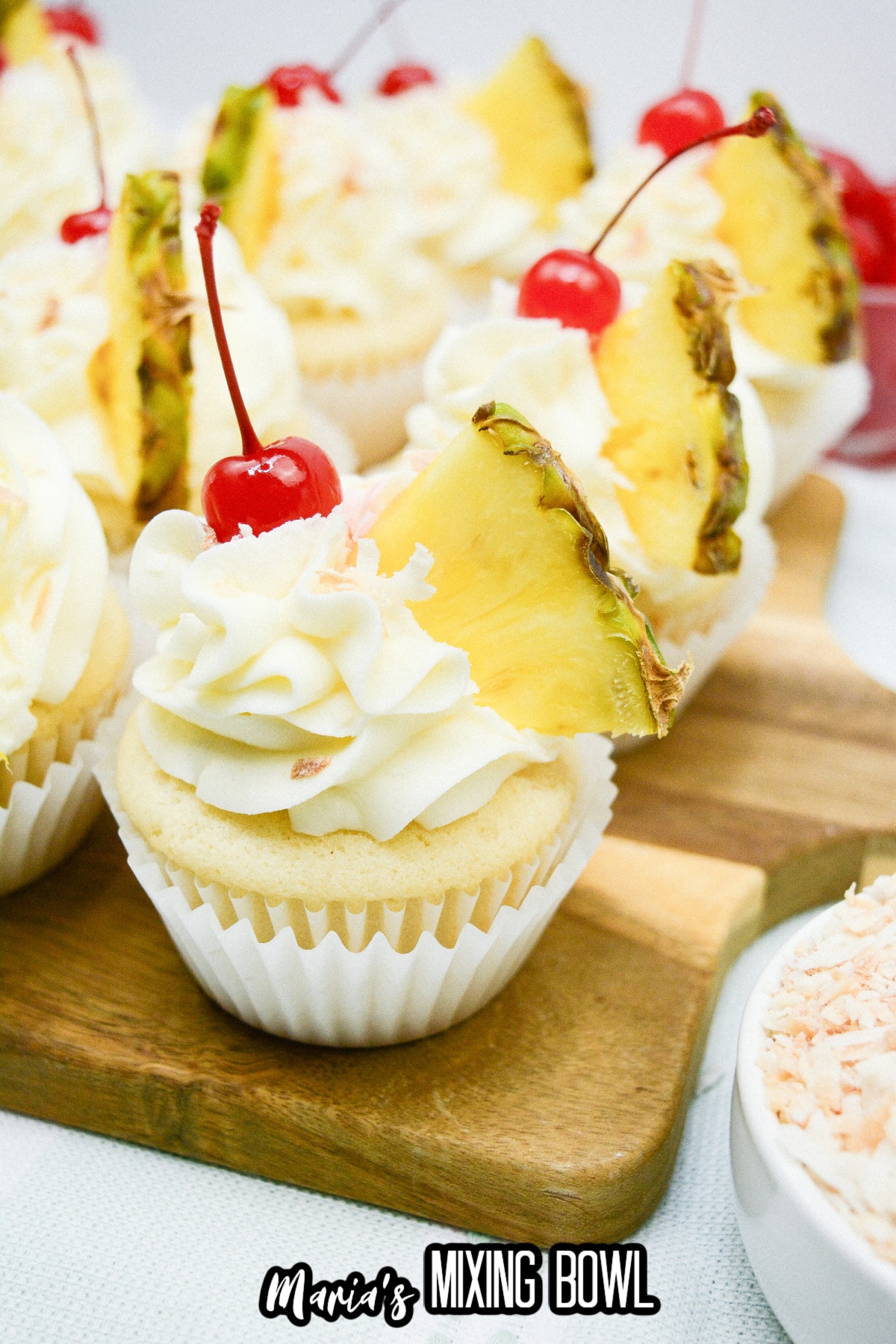 pina colada cupcakes on a wooden cutting board.