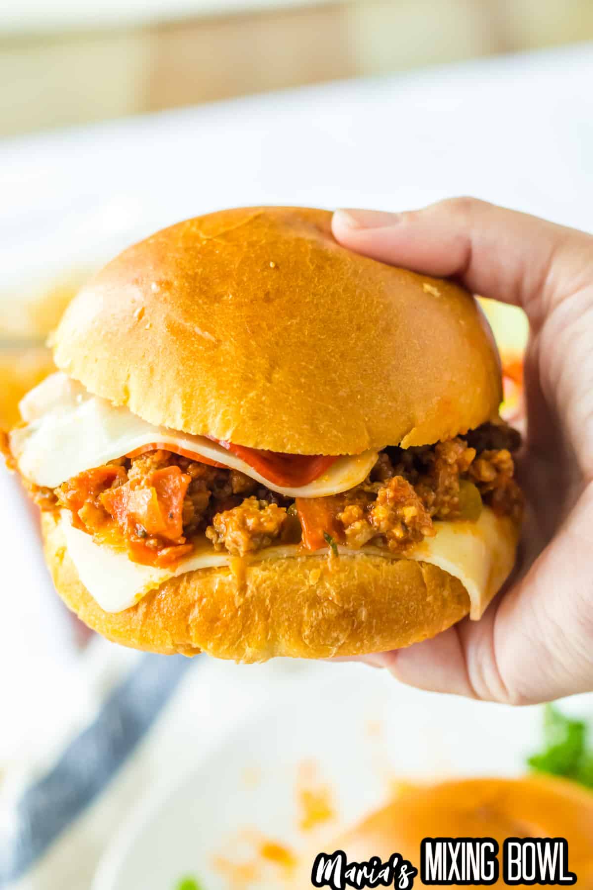 pizza sloppy joe on a bun held in the air in a woman's hand.