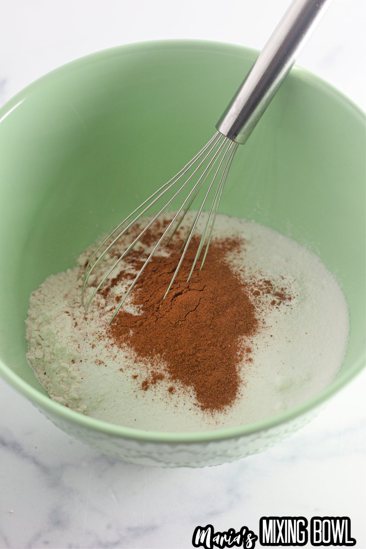 flour, salt, sugar, and pumpkin pie spice being mixed in a large bowl with a whisk.