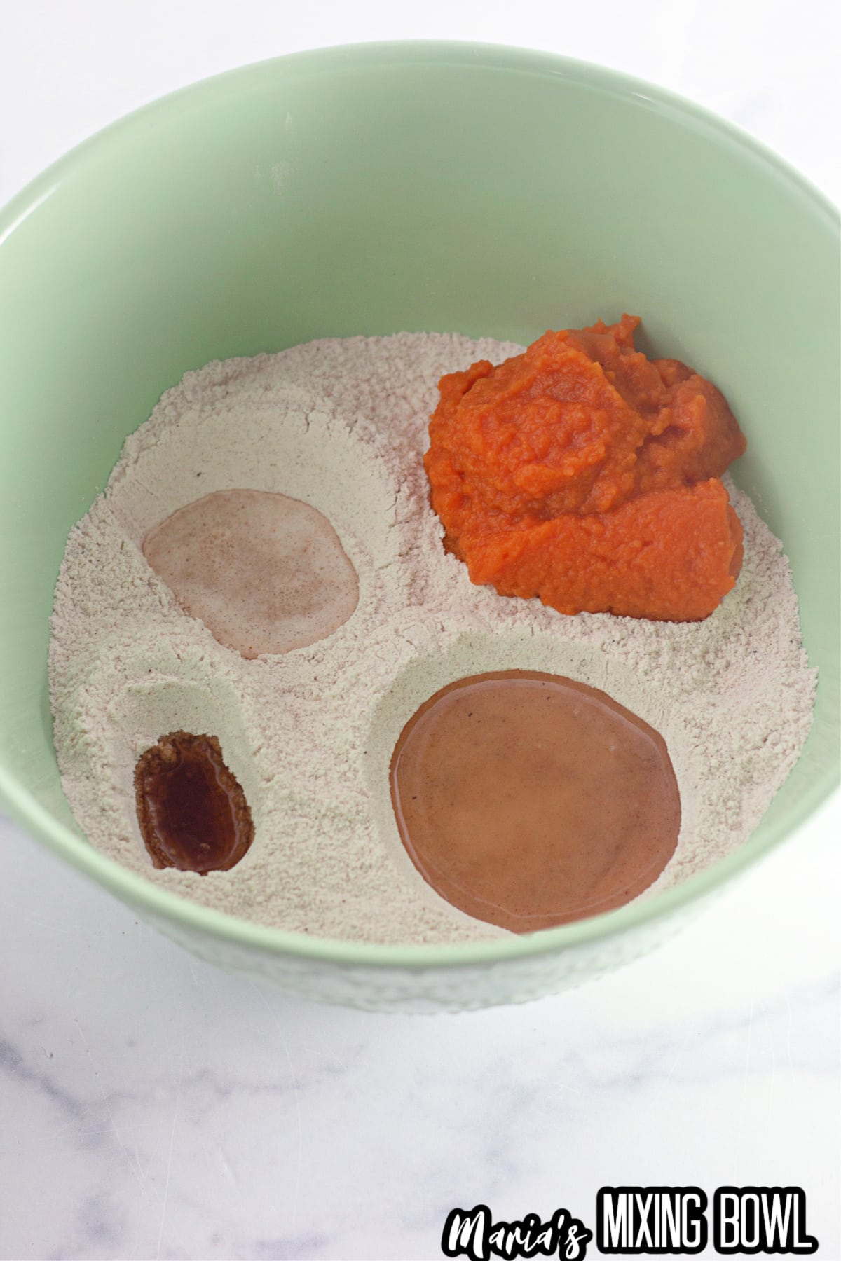 bowl of dry ingredients, with wells that are filled with pumpkin puree, water, vanilla extract, vegetable oil, and white vinegar.