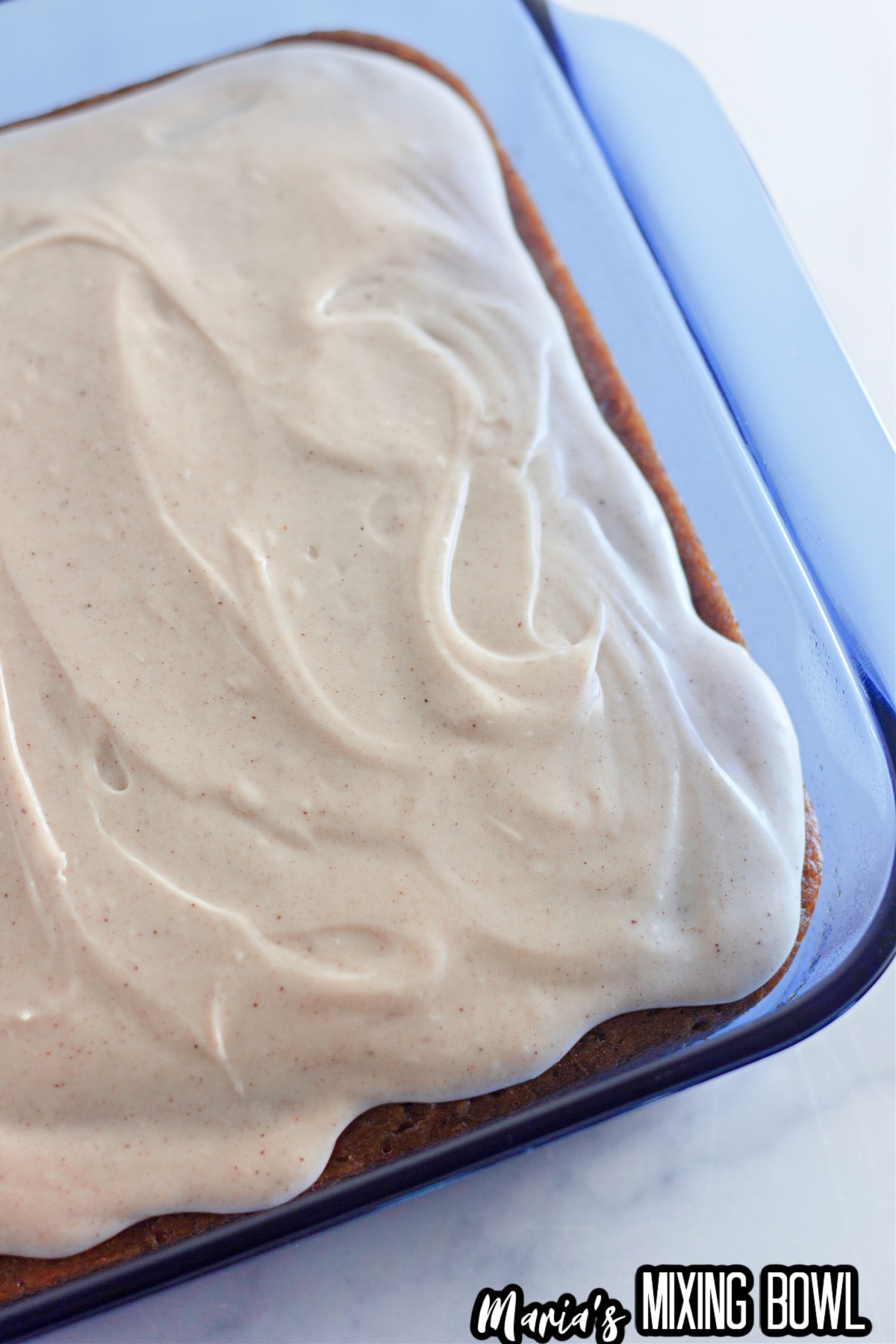 pumpkin crazy cake in a square baking dish topped with cream cheese frosting.