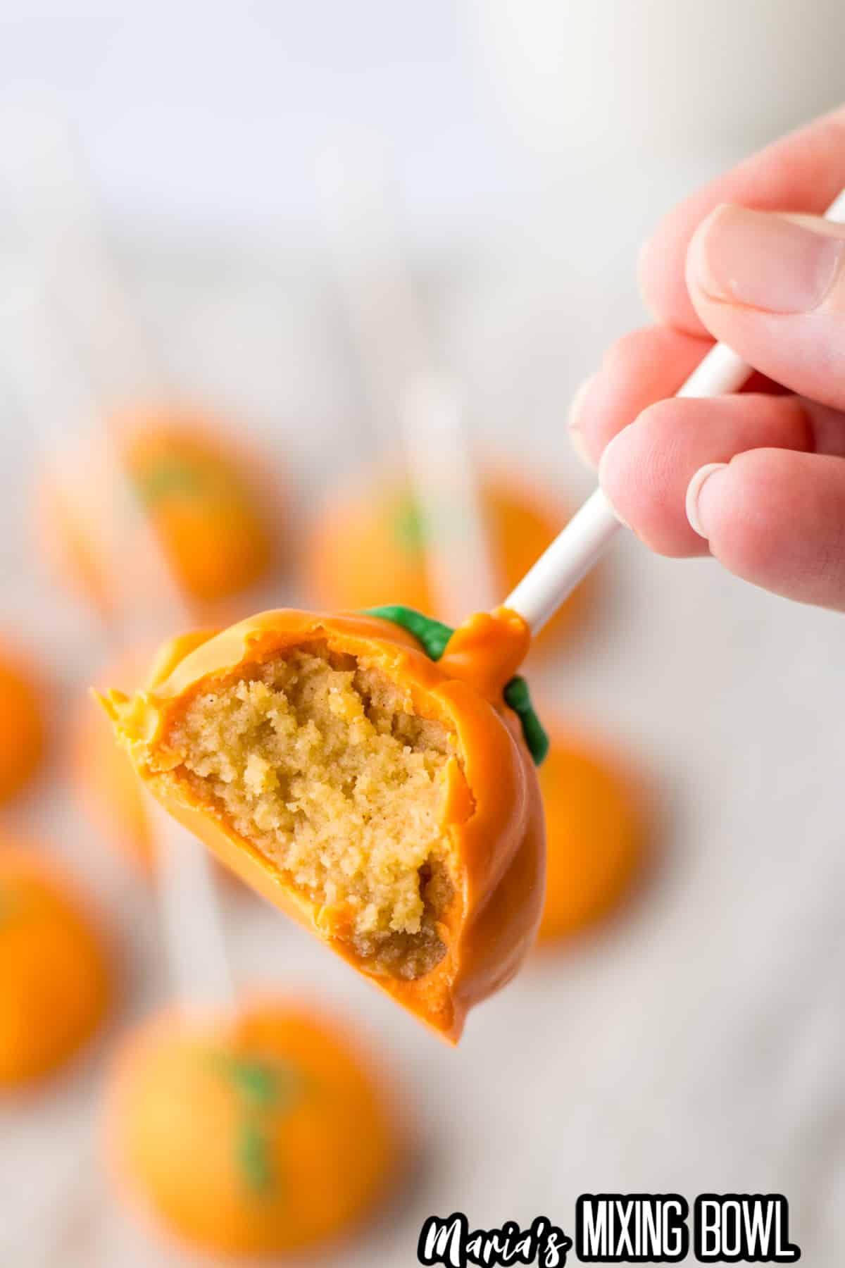 pumpkin oreo truffle on a lollipop stick with a bite missing held in the air.