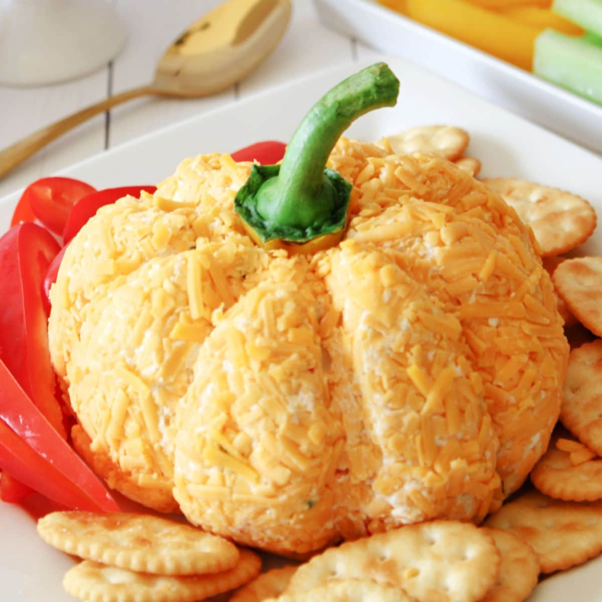 pumpkin shaped cheese ball on a plate with crackers and bell pepper strips.