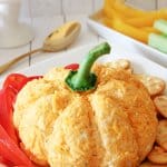 pumpkin shaped cheese ball on a plate with bell pepper slices and crackers.