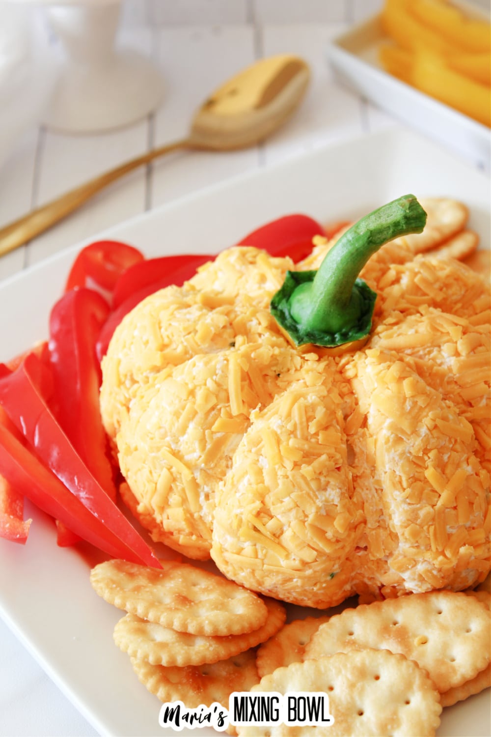 pumpkin shaped cheese ball on a plate with bell pepper slices and crackers.