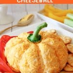 pumpkin shaped cheese ball on a plate with bell pepper slices and crackers.