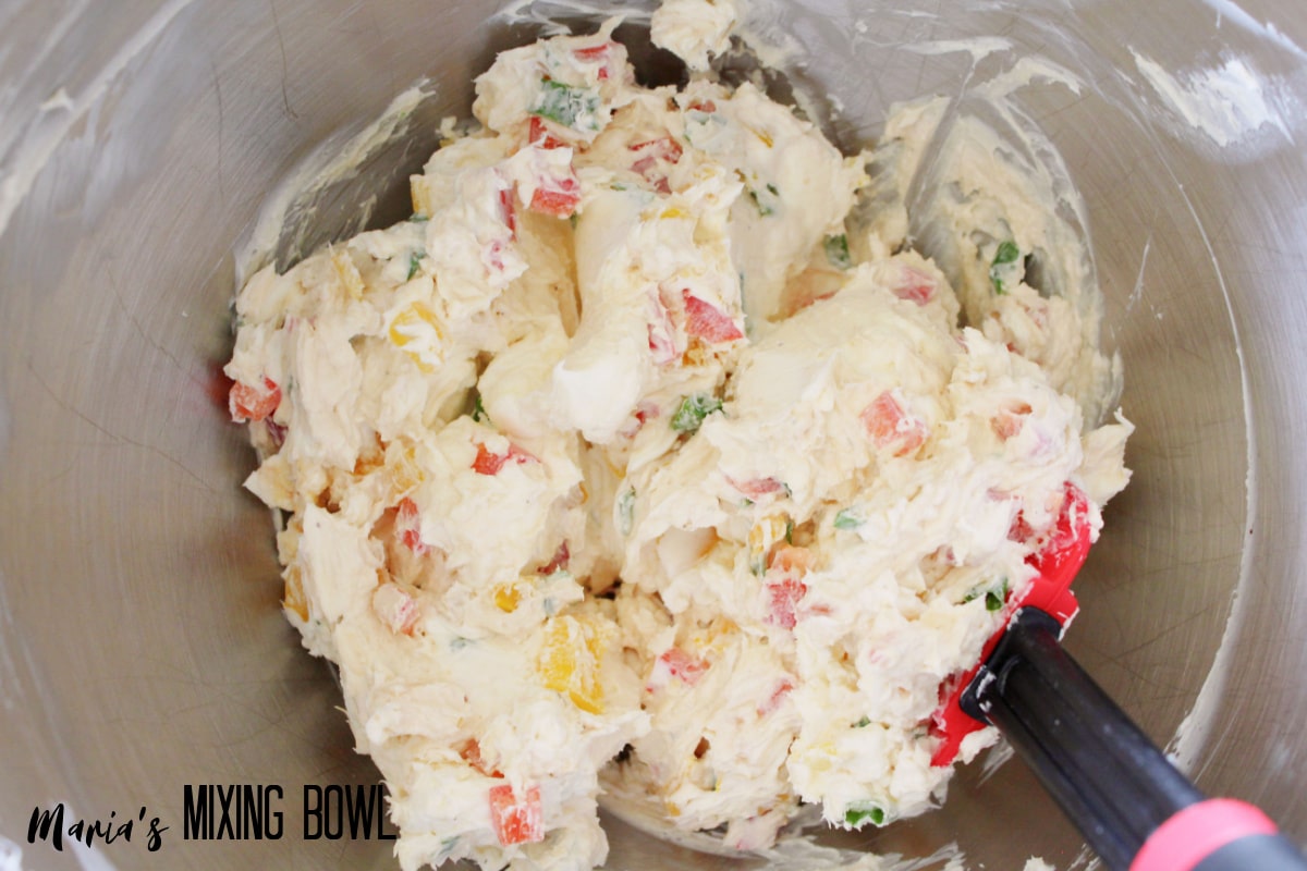 cream cheese, seasonings, and diced peppers being mixed together.