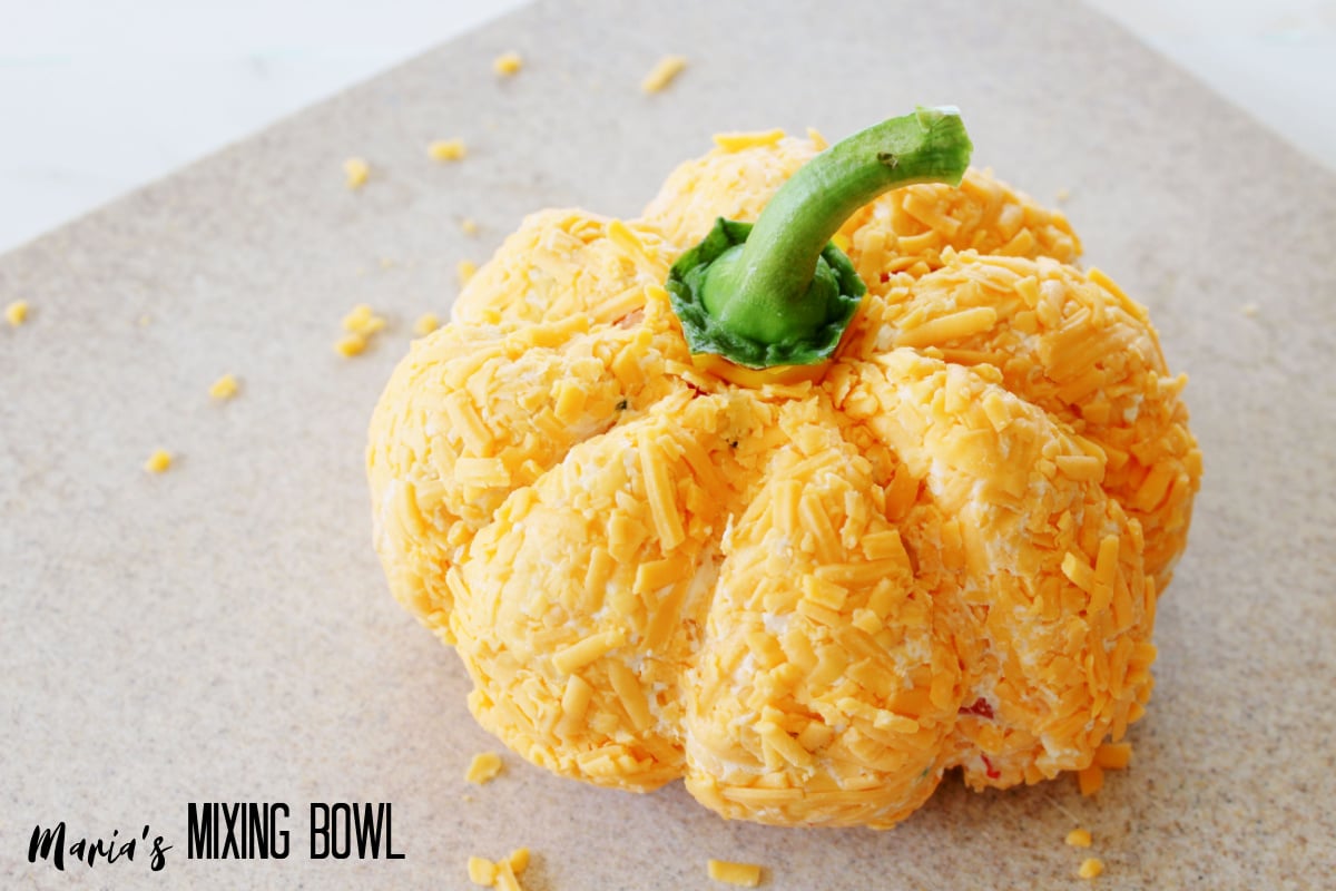 bell pepper stem being added to the top of the pumpkin cheeseball.