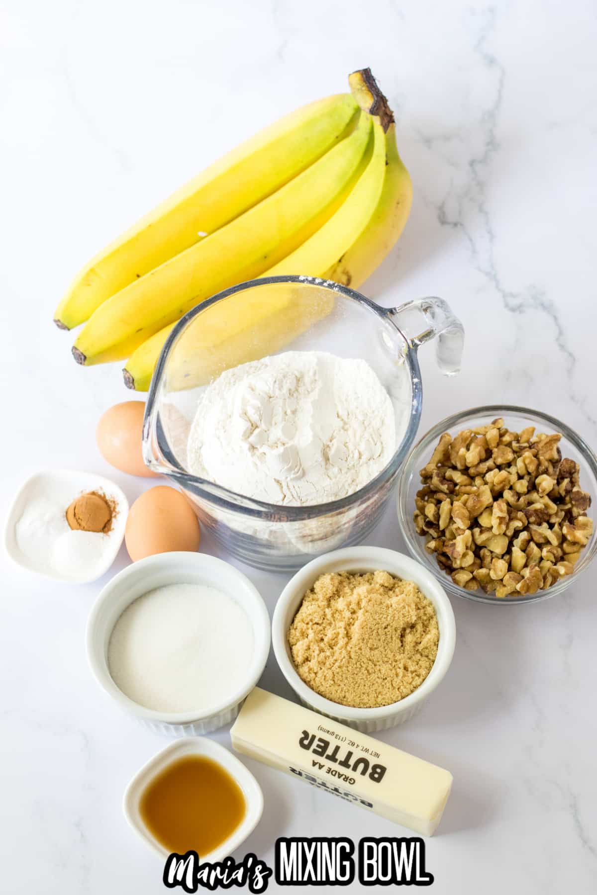 bowls of flour, salt, cinnamon, baking powder, baking soda, chopped walnuts, brown sugar, vanilla extract, granulated sugar, bananas and a stick of butter.