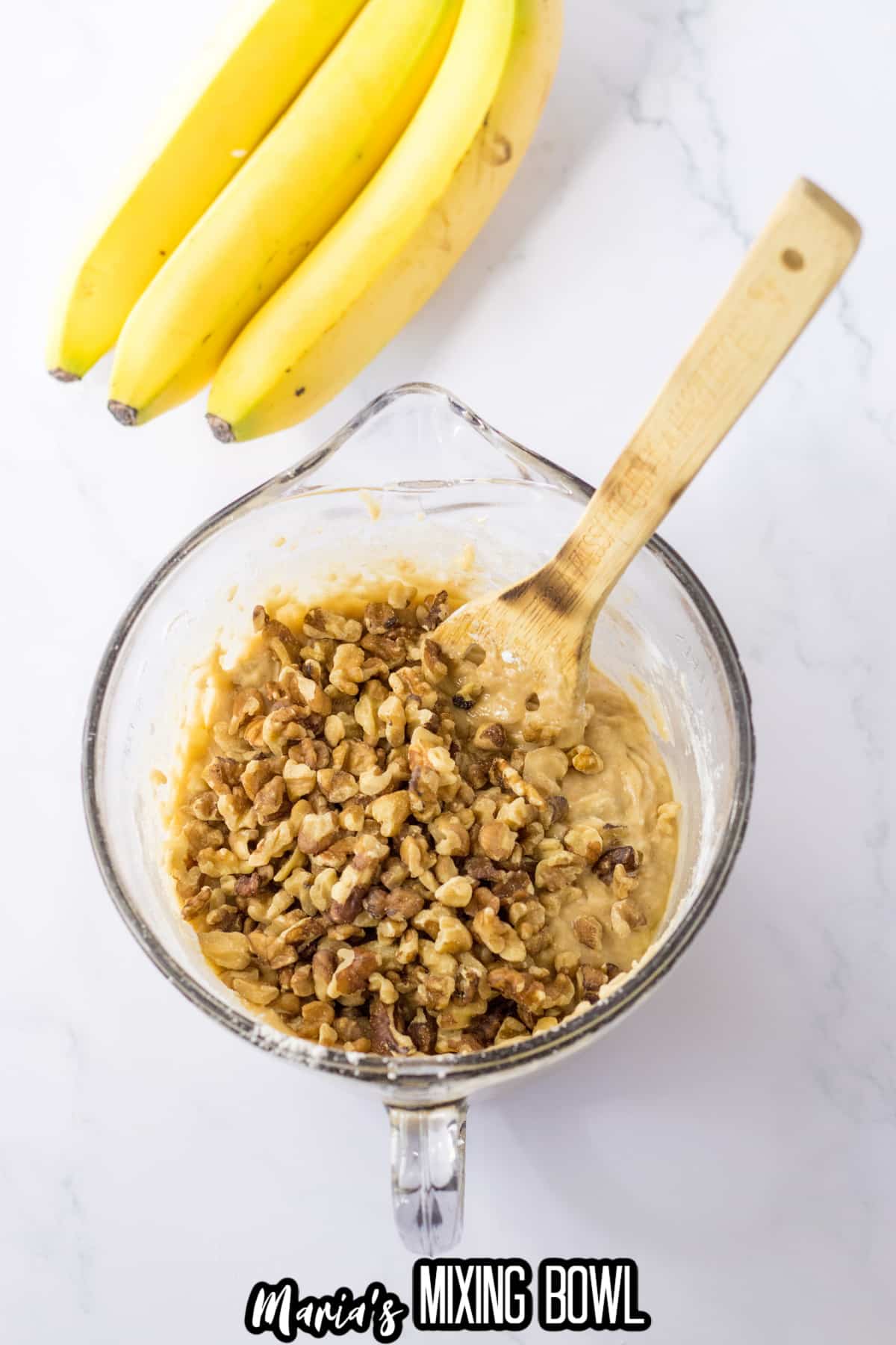 chopped walnuts being stirred into banana bread batter in a large glass mixing bowl.