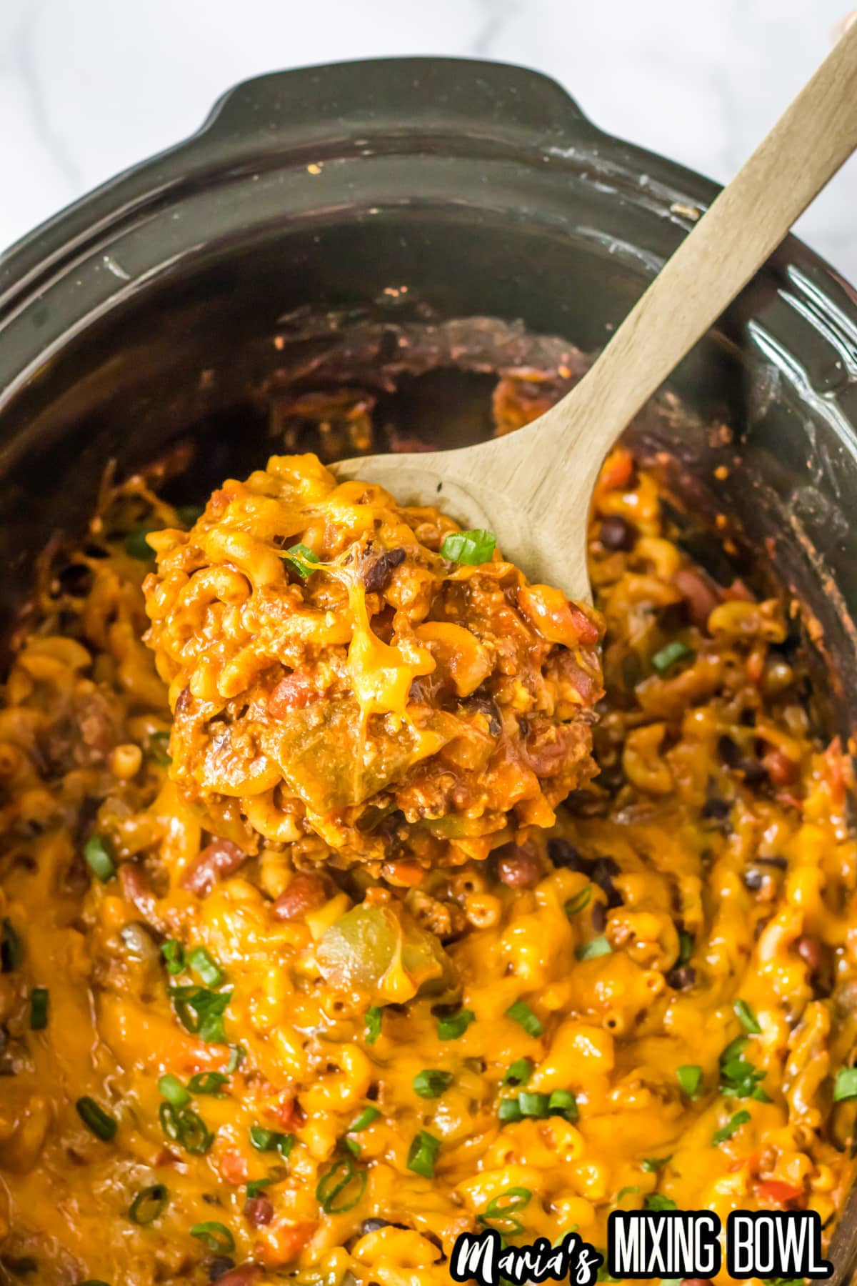 wooden spoonful of chili mac being taken out of the slow cooker.