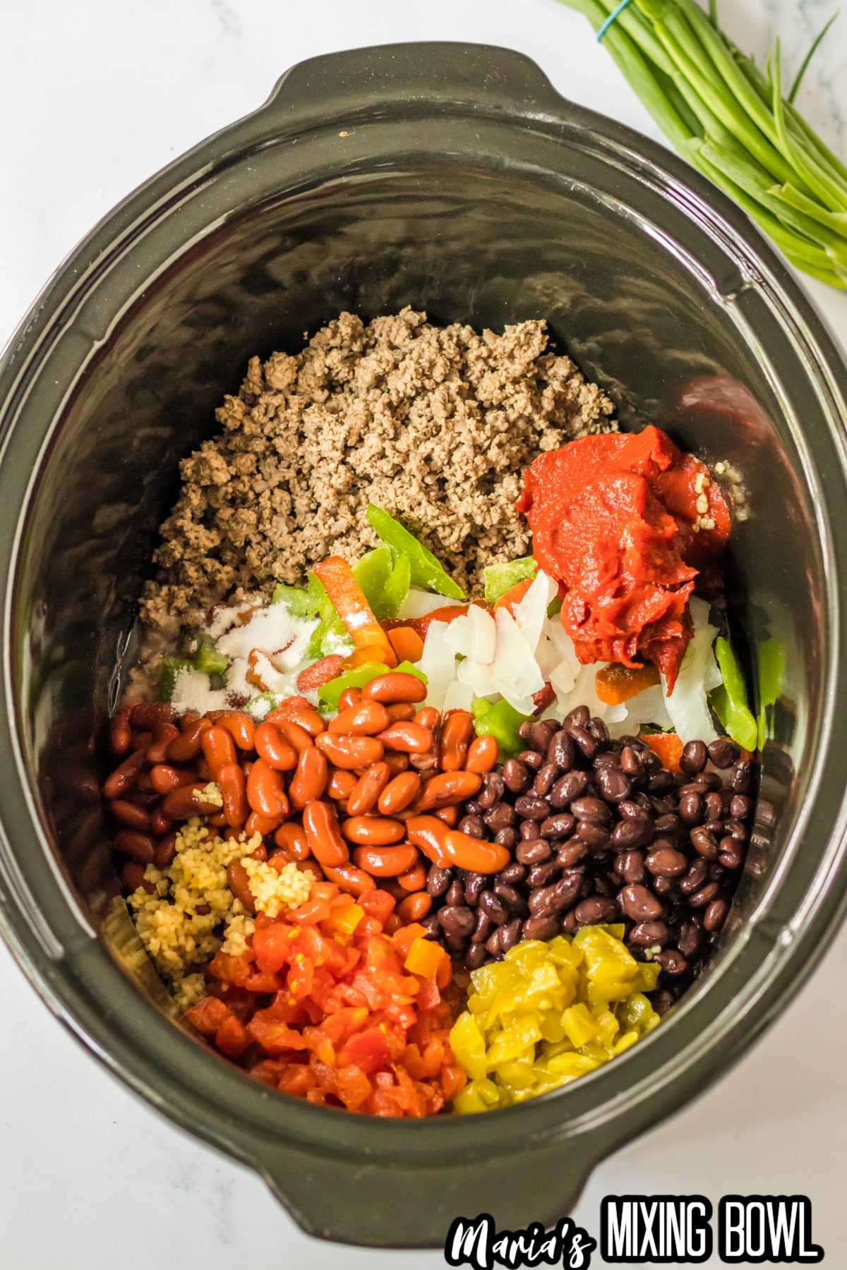 ground beef, tomato paste, onions, bell peppers, beans, garlic, and peppers in a slow cooker.