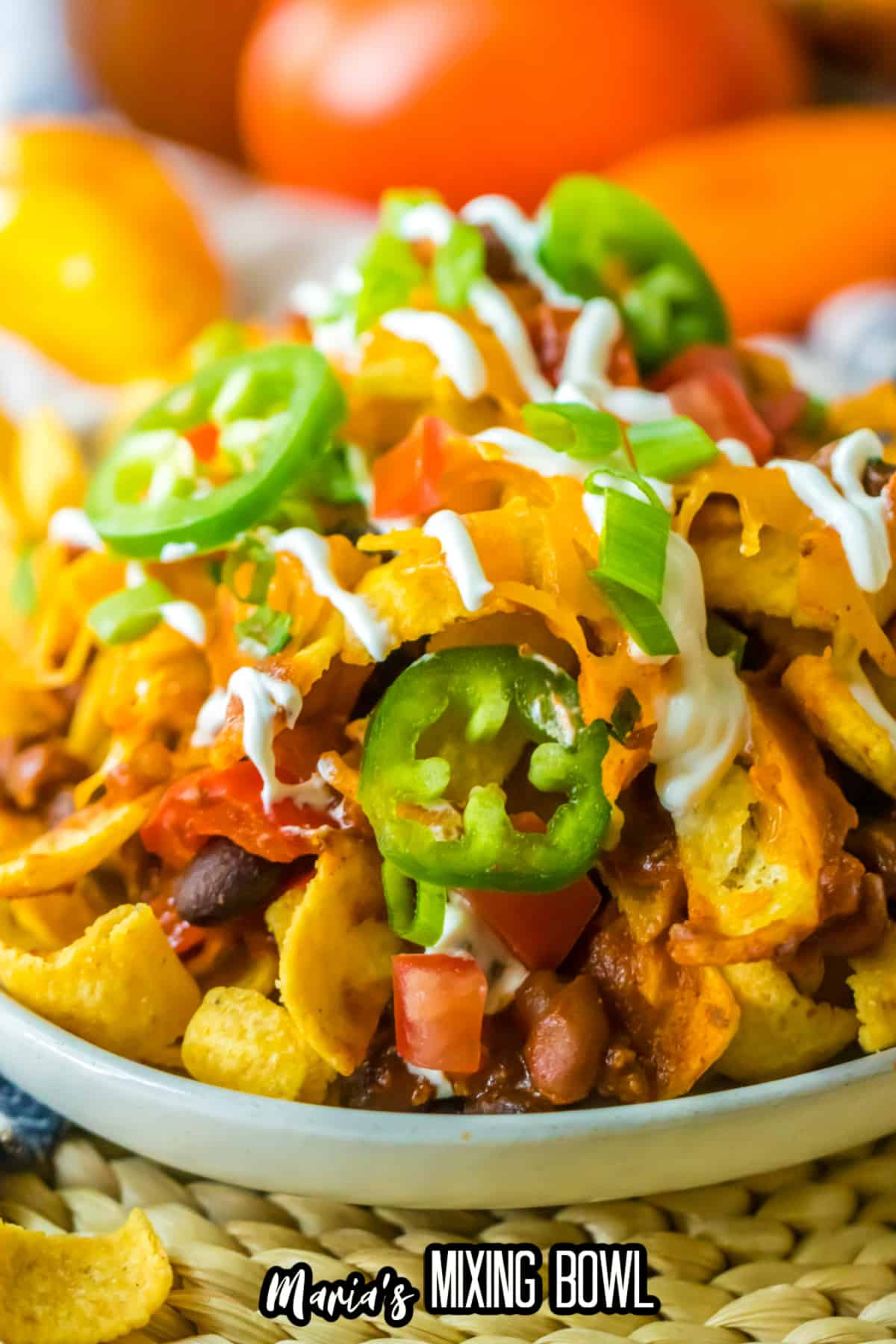 plate full of frito pie and topped with jalapeno slices and sour cream.