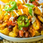 plate full of frito pie and topped with jalapeno slices and sour cream.
