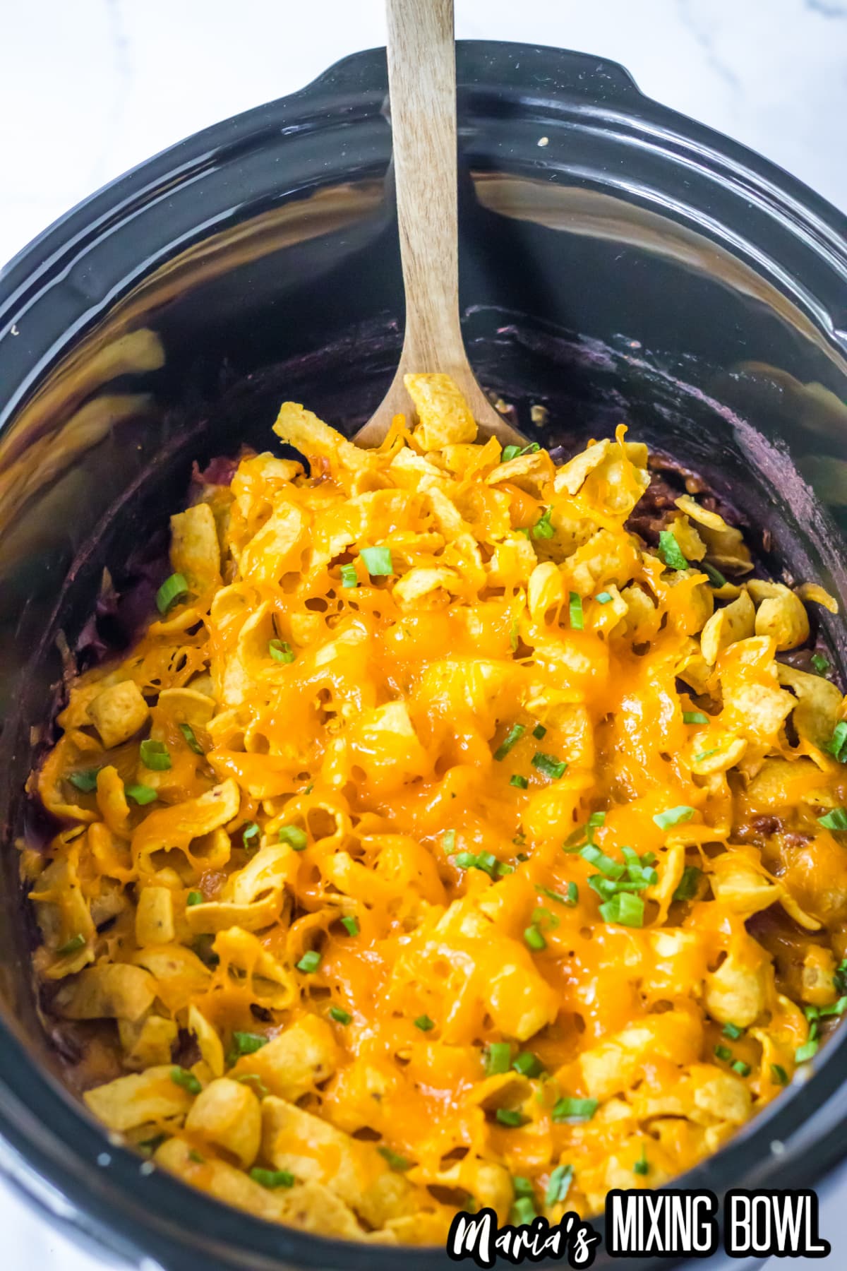frito pie topped with corn chips and cheese in a slow cooker.