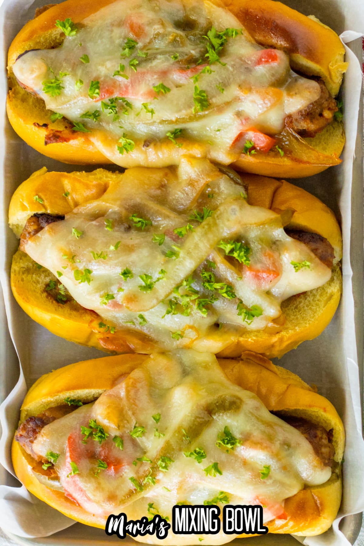 sausage and peppers on a hoagie roll with melted cheese on top on a metal serving tray.
