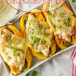 sausage and peppers on a hoagie roll with melted cheese on top on a metal serving tray.