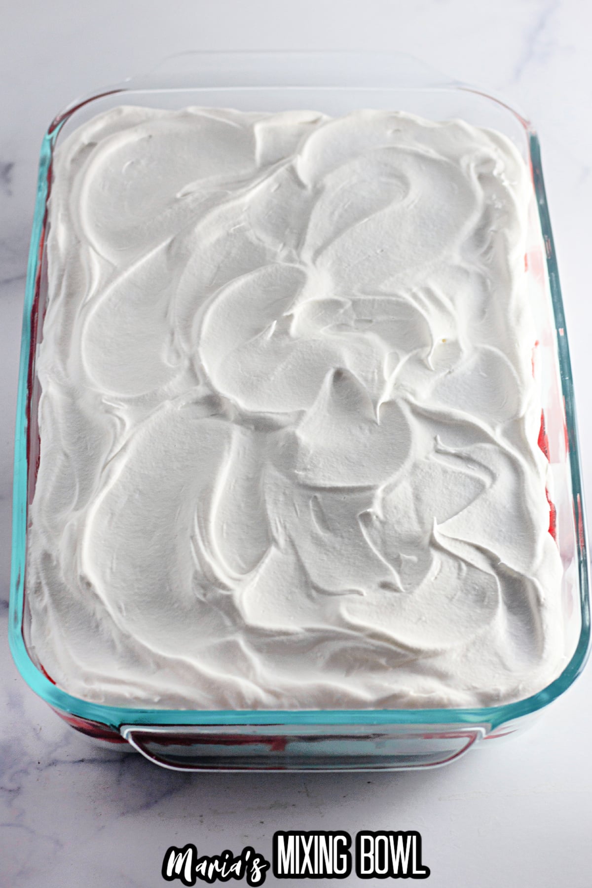 Cool whip being spread on top of the strawberry ice cream cake.