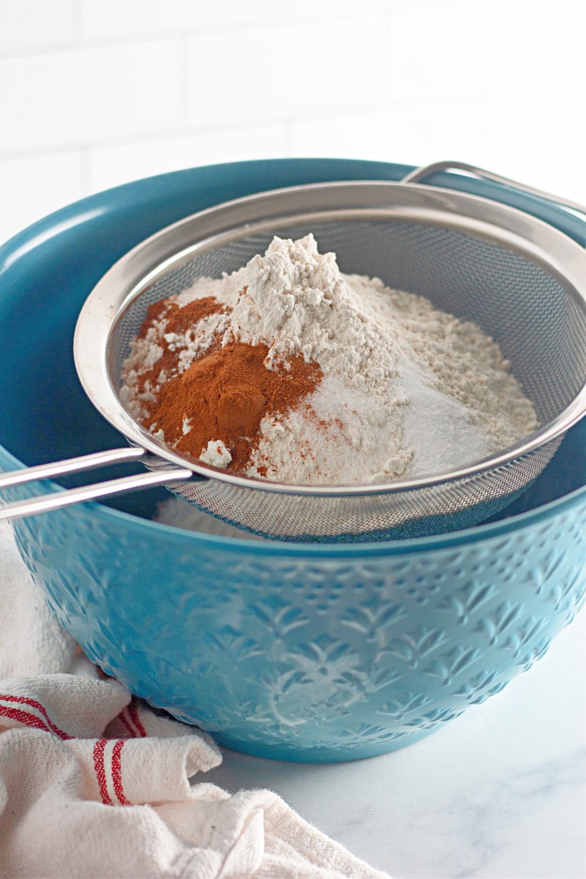 flour, cinnamon , baking soda in a sifter held over a bowl.
