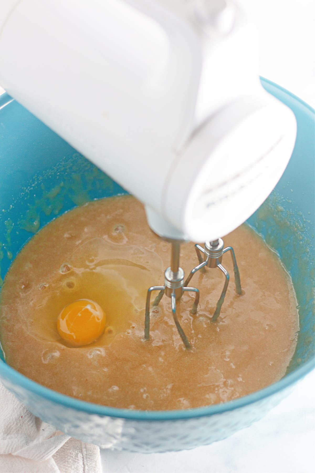 butter, sugar, and eggs being beaten with a hand mixer in a mixing bowl.