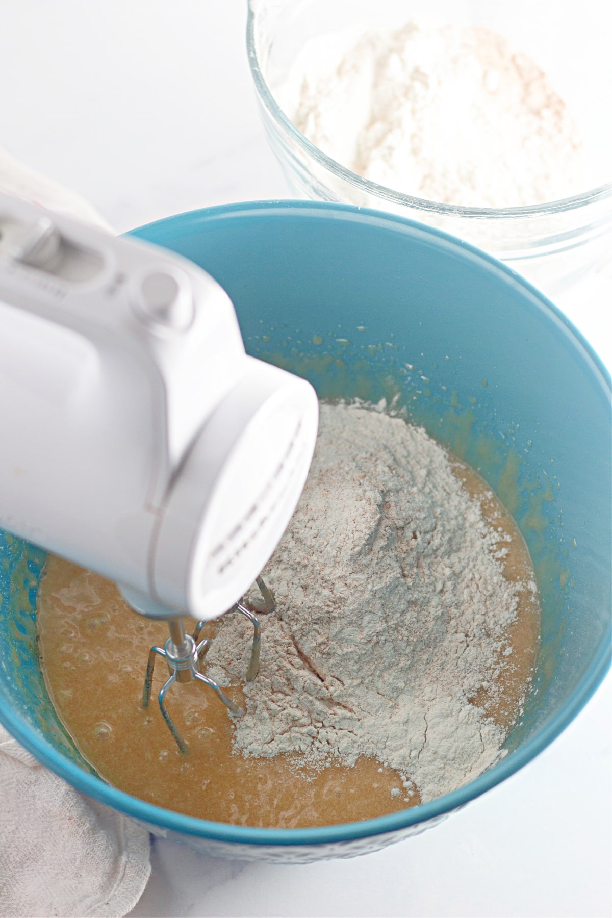 flour mixture being added to the apple cake batter with a hand mixer in a bowl.