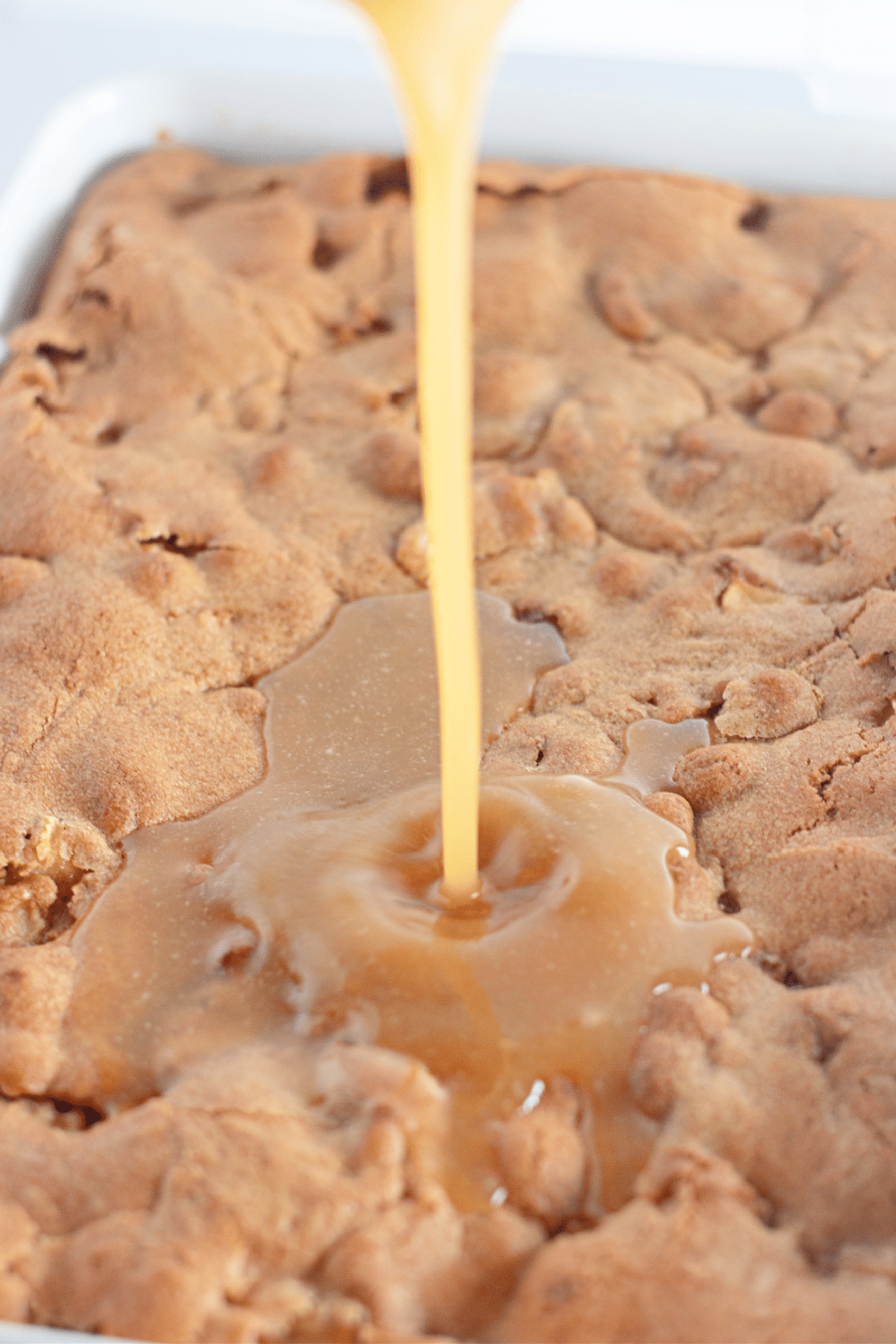 frosting being poured on top of a warm baked cake.