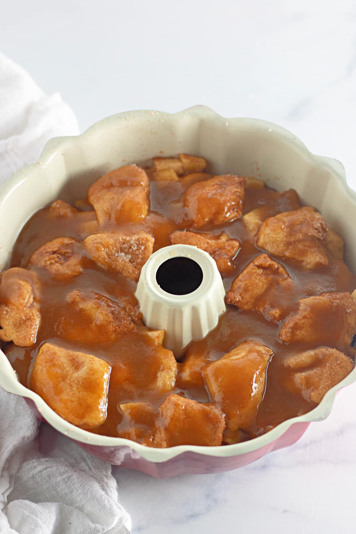 raw monkey bread topped with caramel sauce in a bundt pan.