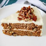 slice of apple spice cake topped with cream cheese frosting on a white plate.