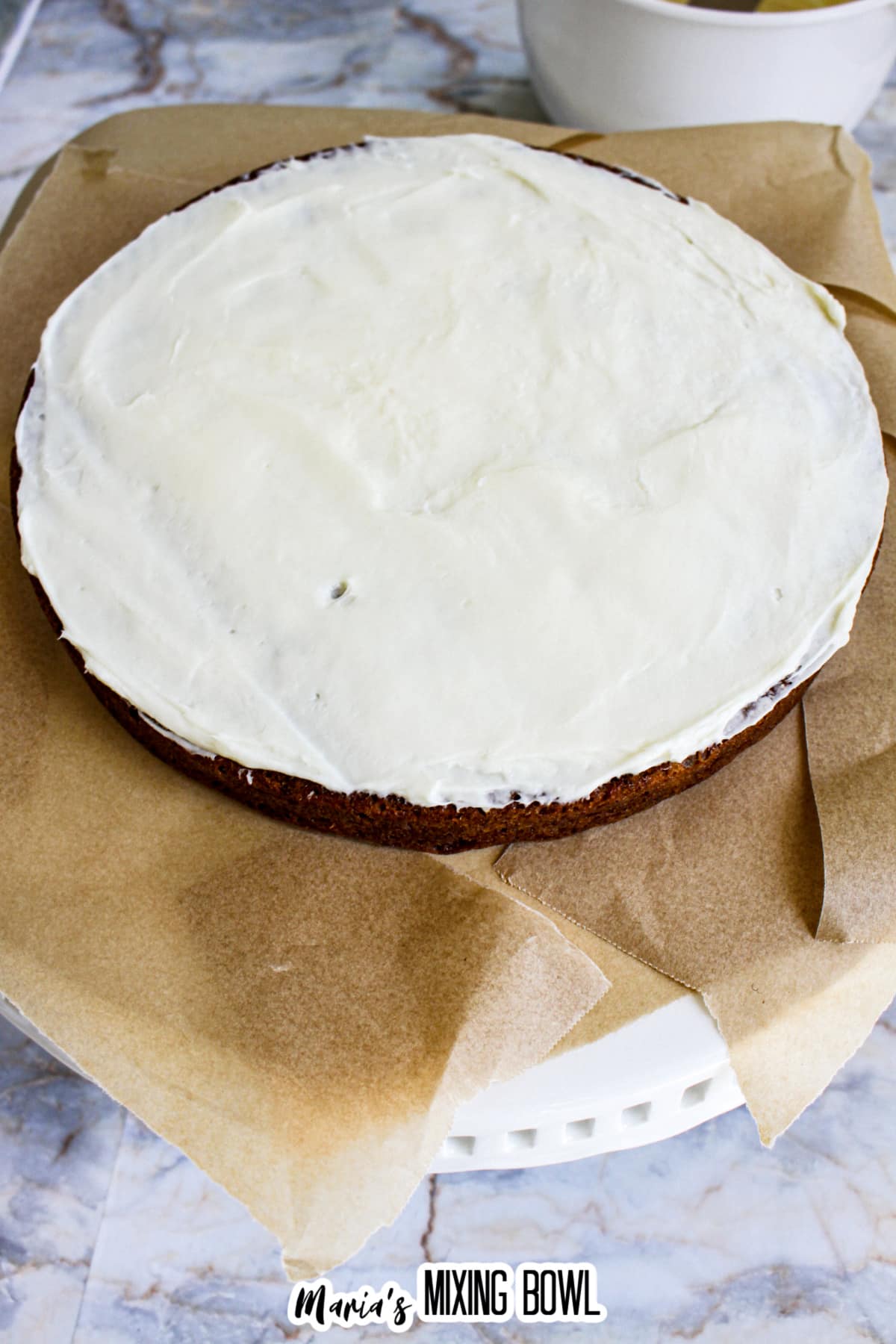 cream cheese frosting being spread on the first layer of an apple cake.