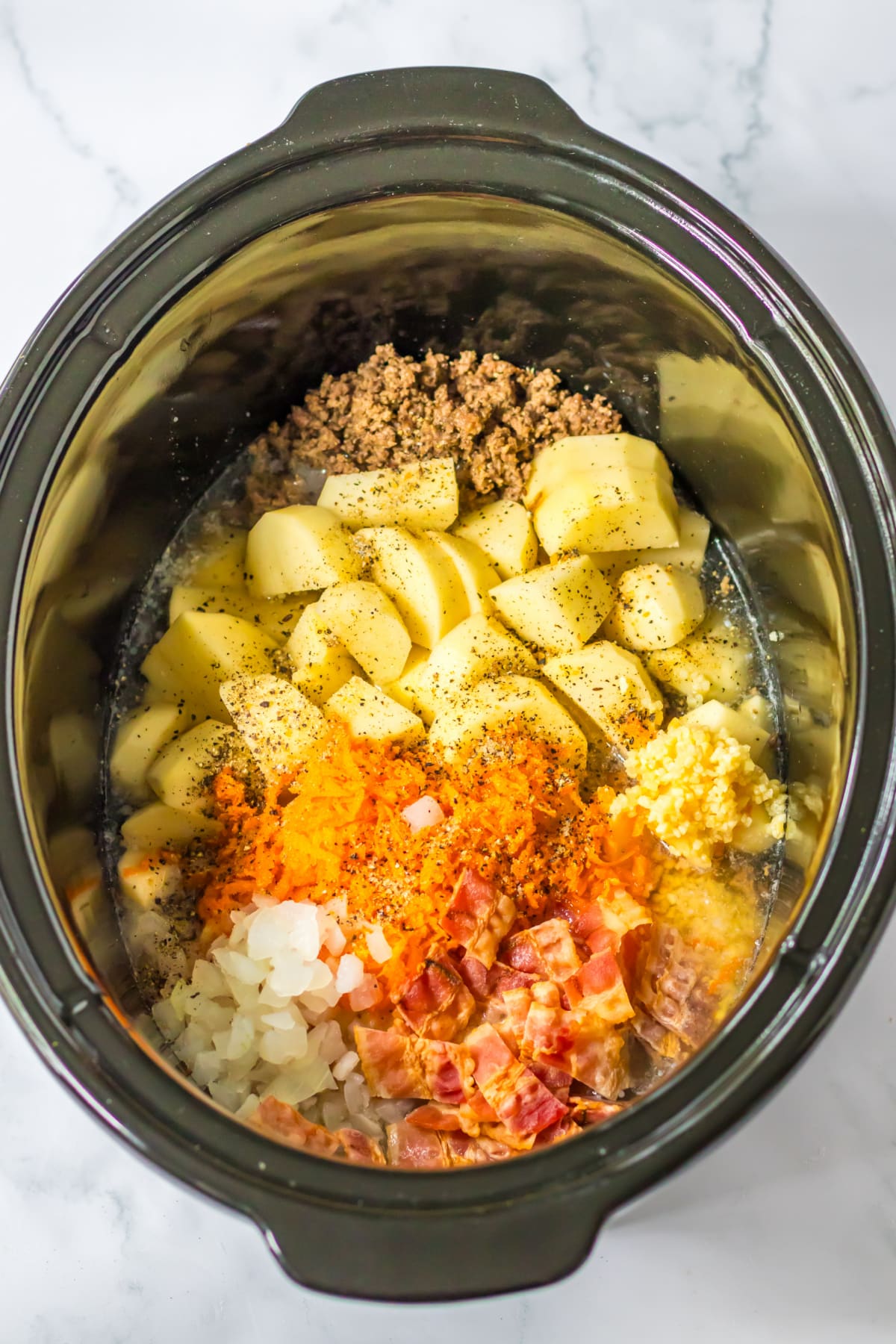 ground beef, potatoes, onions, bacon, chicken broth, and seasonings in a slow cooker.