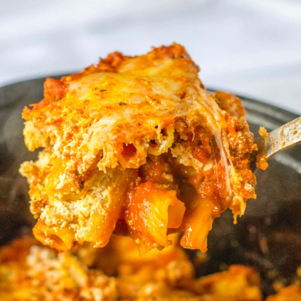 spoon full of baked ziti held above a slow cooker.