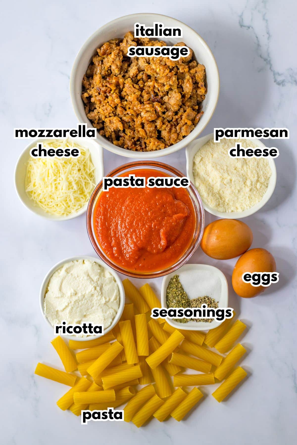 bowls of italian sausage, parmesan cheese, mozzarella cheese, pasta sauce, eggs, ricotta cheese, seasonings, and pasta.