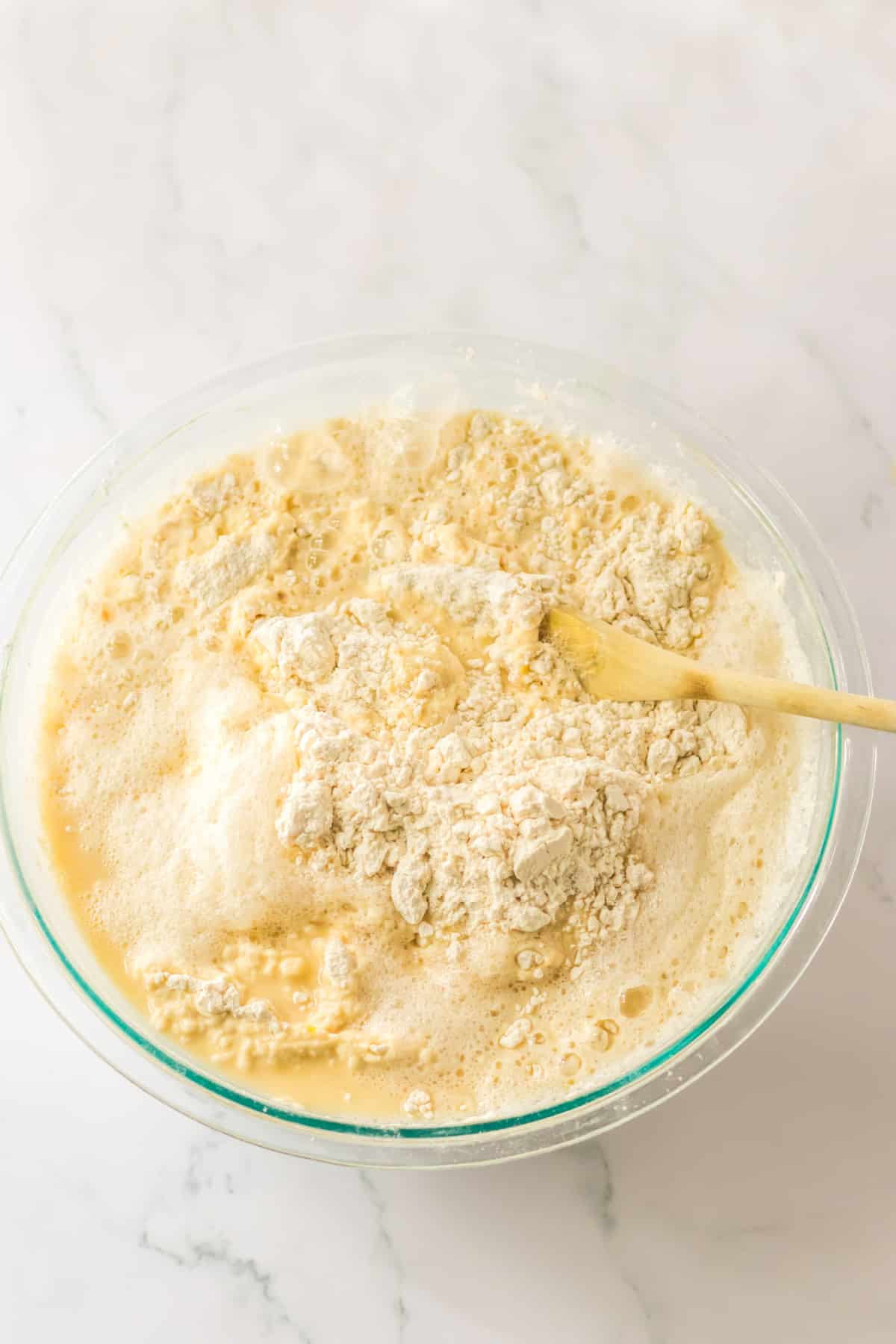 wet and dry ingredient being mixed to make roll dough in a glass bowl.