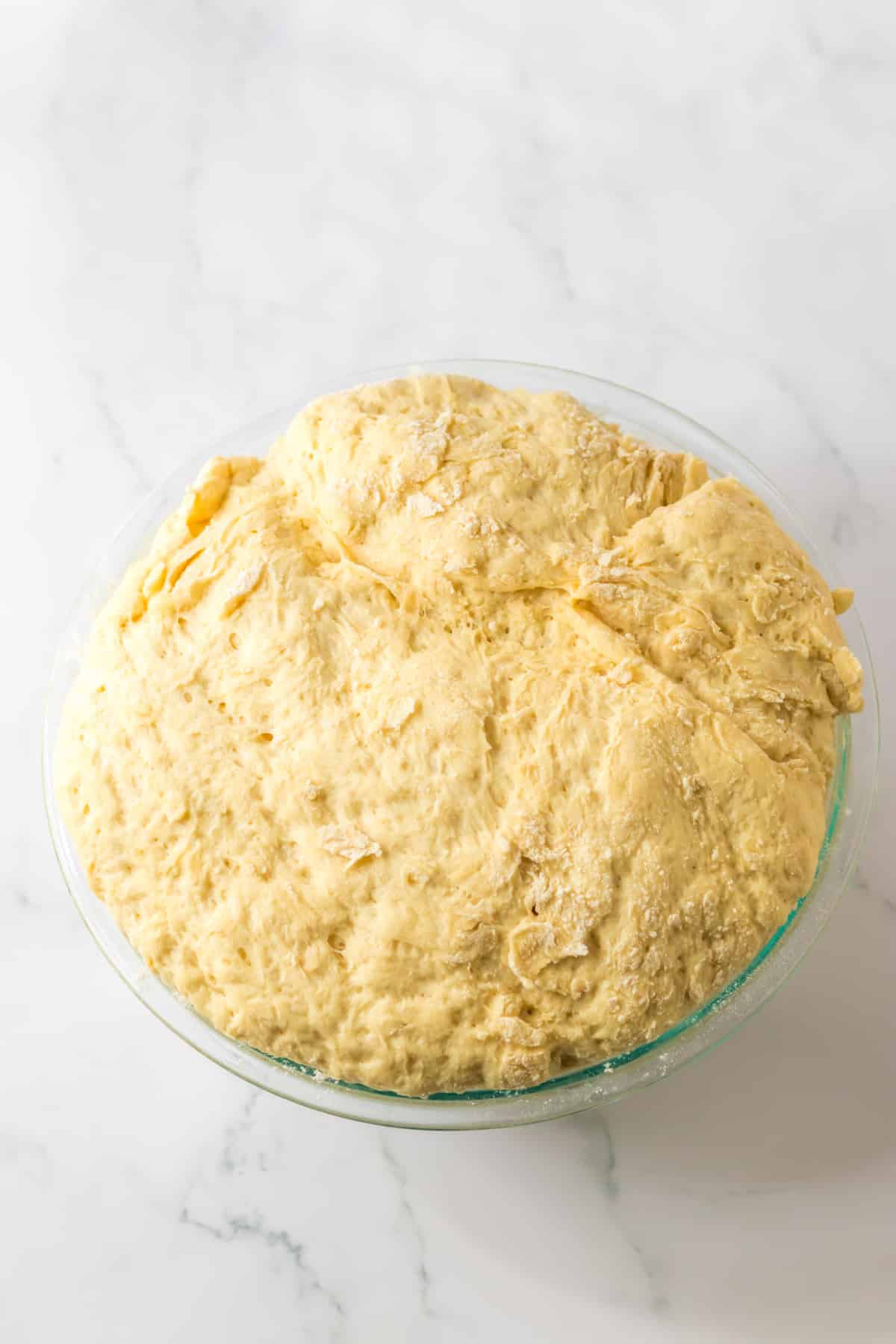 roll dough rising in a glass mixing bowl.