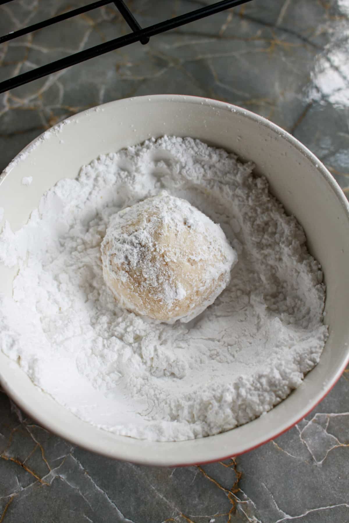 cherry snowball cookie being rolled in powdered sugar.