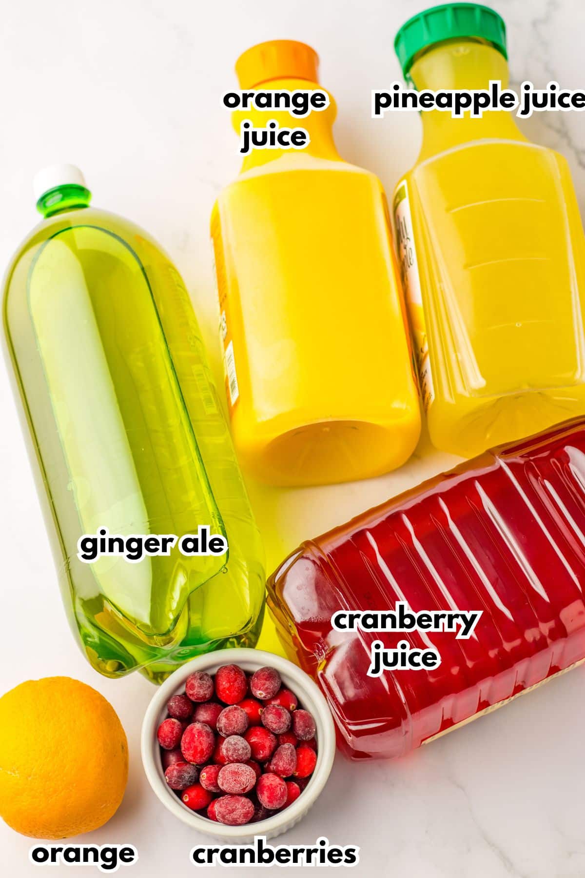 bottles of ginger ale, orange juice, pineapple juice, cranberry juice, an orange and a bowl of cranberries on a counter.