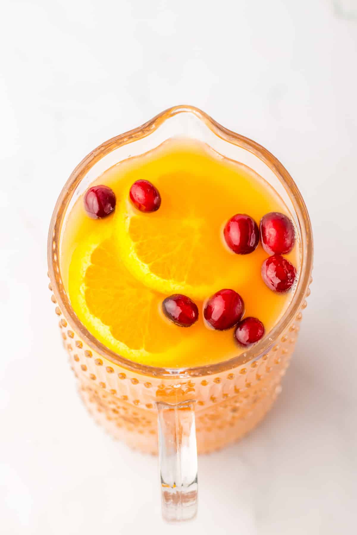 glass pitcher full of punch with orange slices and whole cranberries added for garnish.