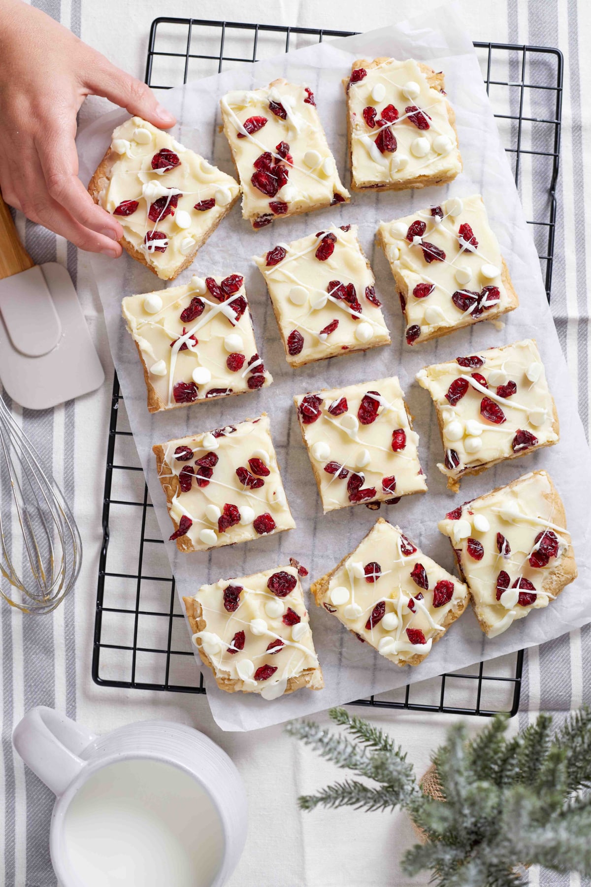 cranberry bliss bars decorated and cut on a wire rack with a woman's hand removing one of the bars.