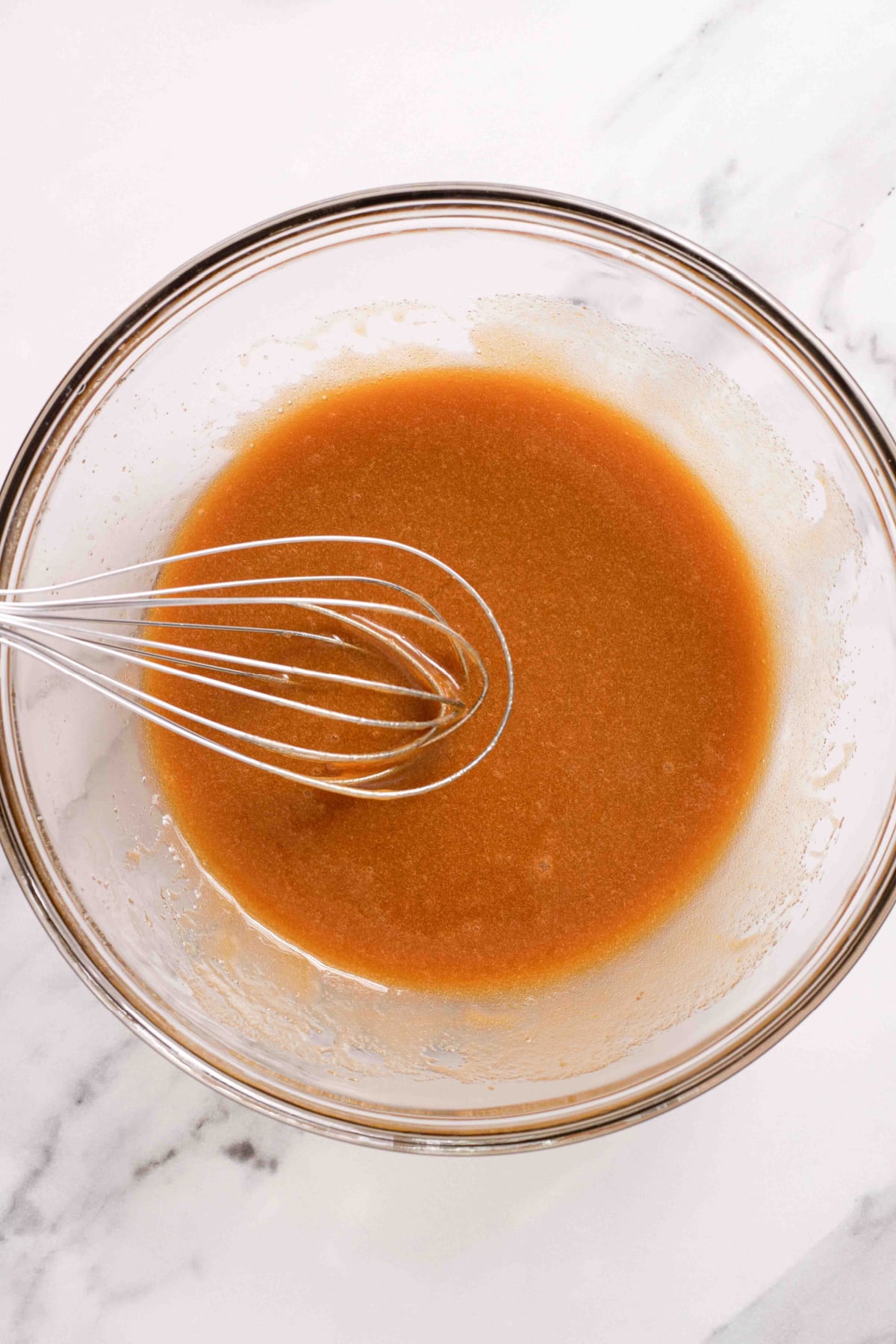 wet ingredients being mixed together in a glass mixing bowl.
