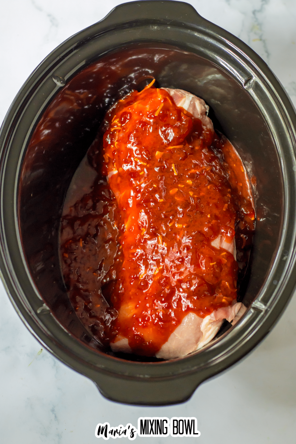 raw pork loin in a slow cooker topped with cranberry sauce.