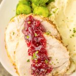 slices of cranberry turkey roast, mashed potatoes and steamed brussels sprouts on a plate.