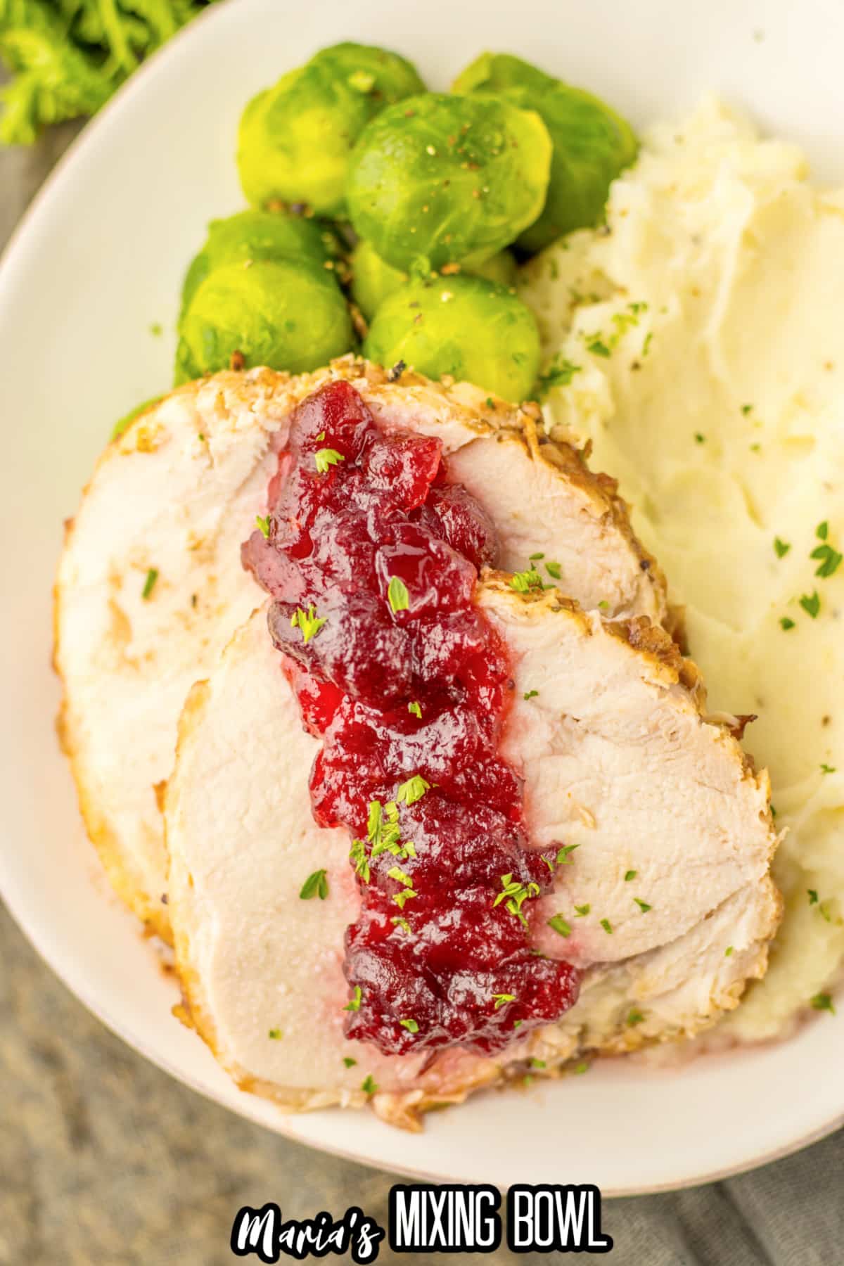 slices of cranberry turkey roast, mashed potatoes and steamed brussels sprouts on a plate.