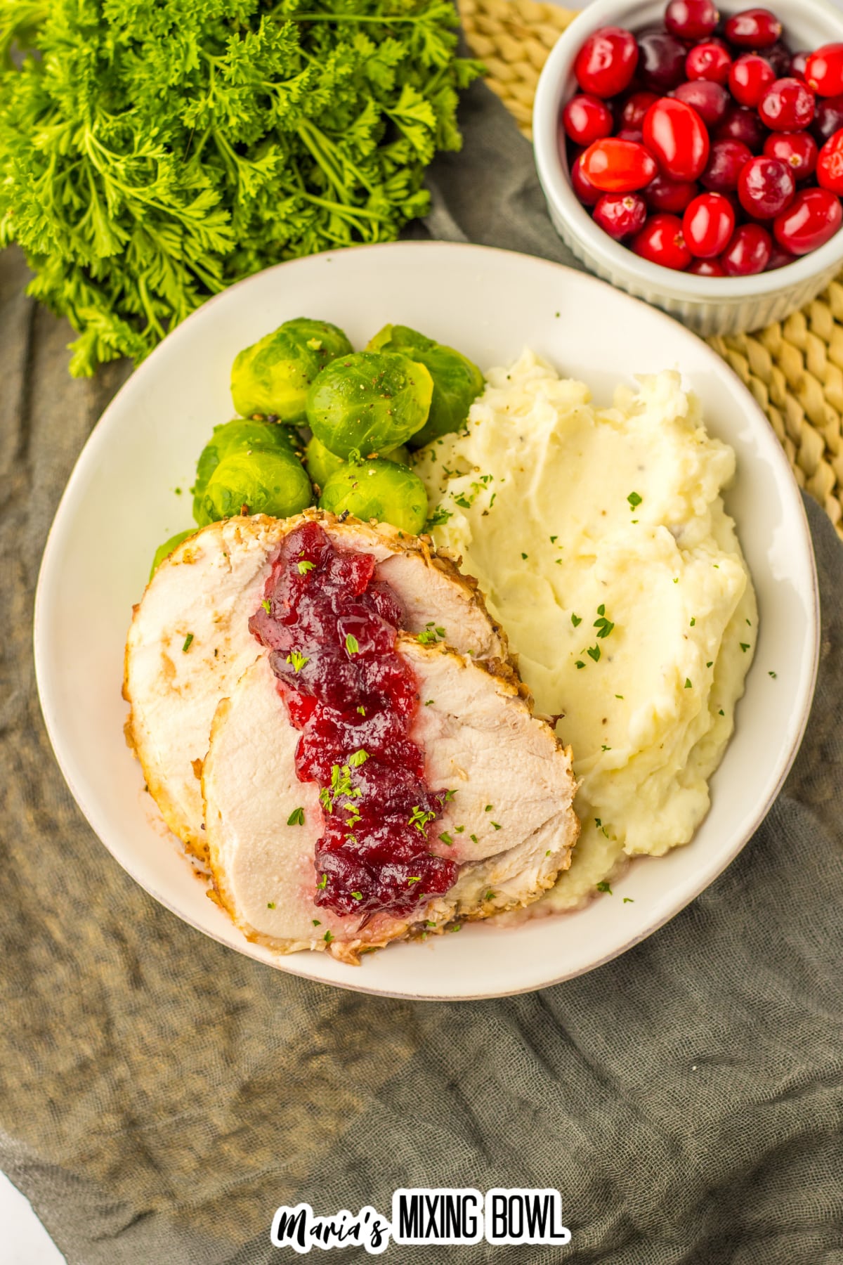 slices of cranberry turkey roast, mashed potatoes and steamed brussels sprouts on a plate.