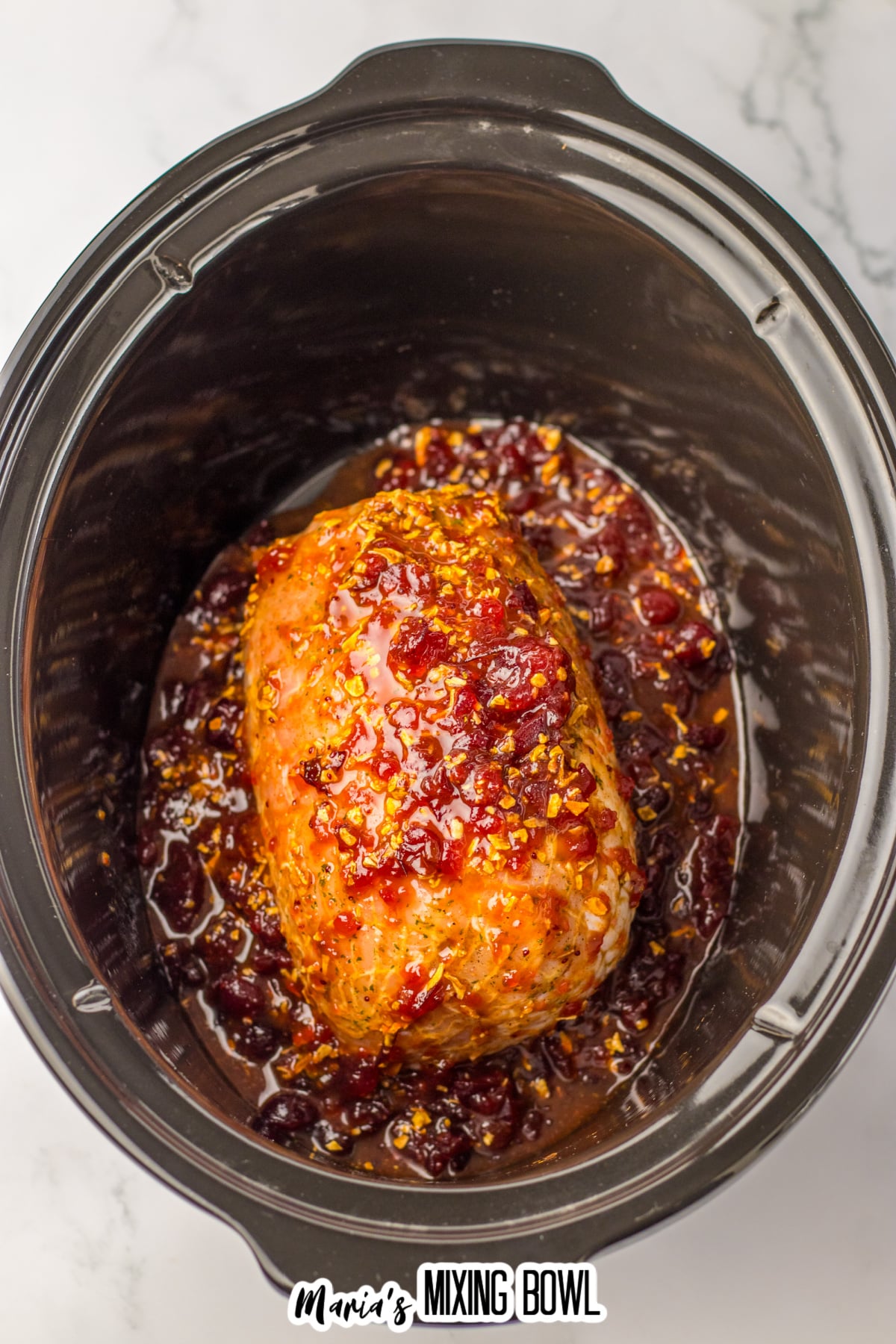 raw turkey roast coated in cranberry sauce in the slow cooker.