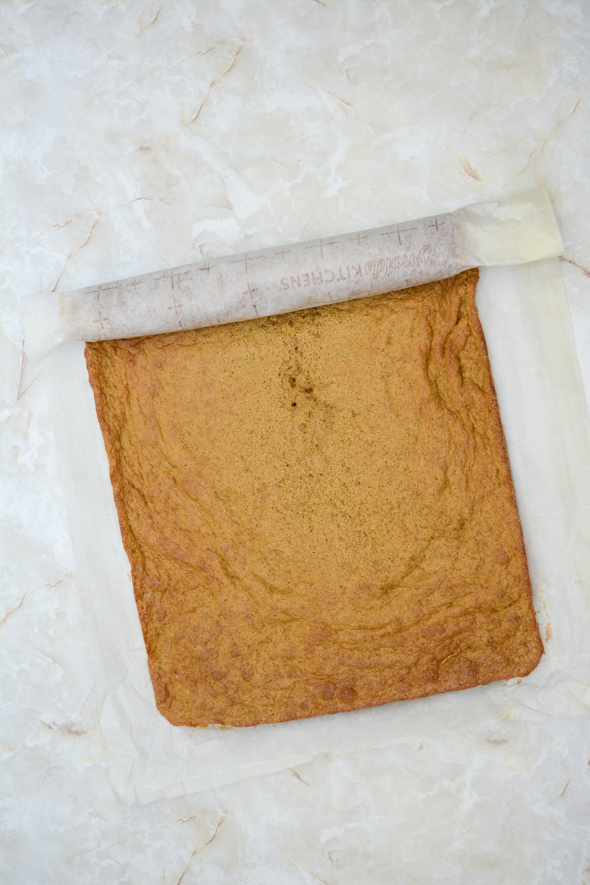 warm cake being rolled in parchment paper.